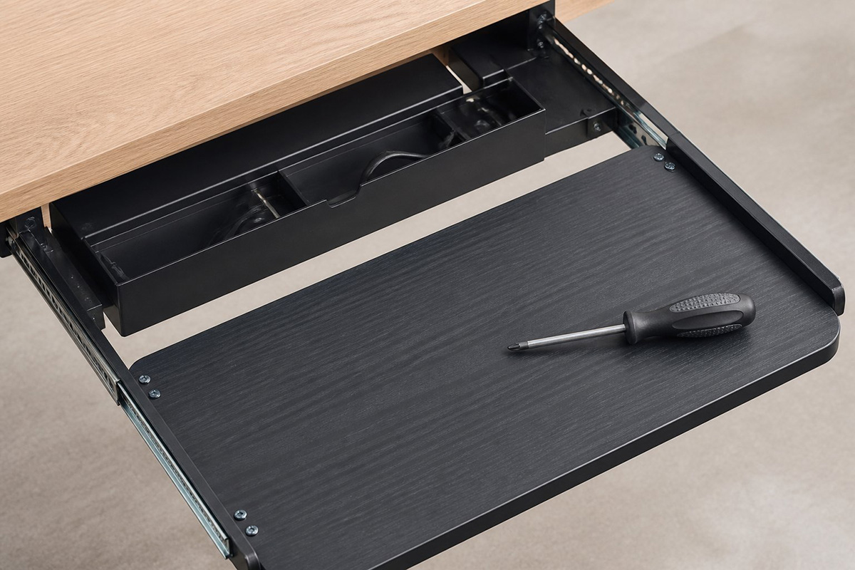 Close-up of computer desk assembly showing keyboard tray and cable channels